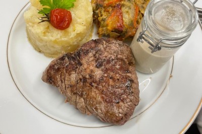 Assiette composée d'un steak grillé, d'une purée garnie, d'un gratin de légumes et d'une sauce en pot individuel.