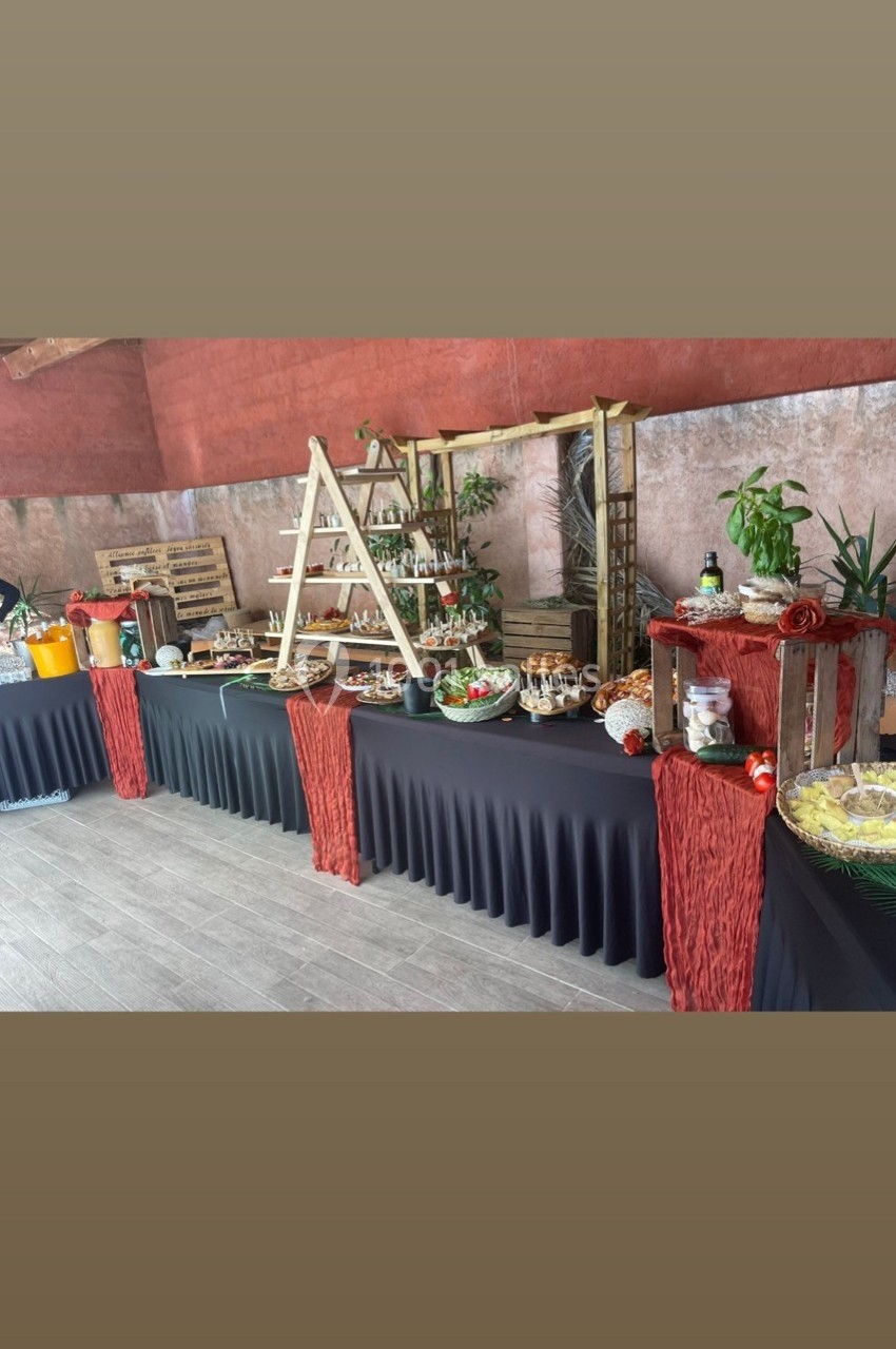 Buffet varié avec plats, boissons et décorations végétales sur des tables drapées de noir dans un espace intérieur.