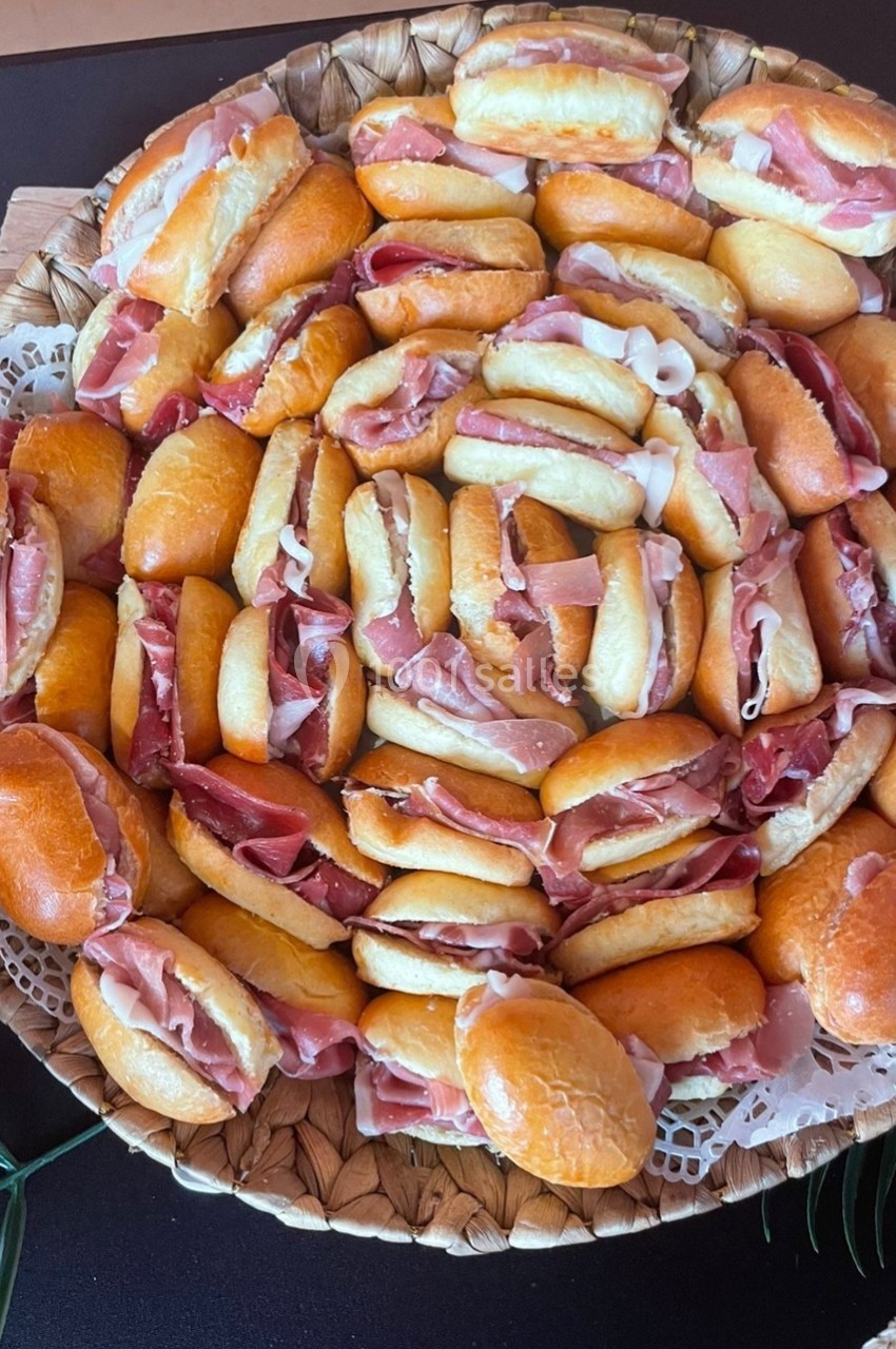 Plateau de petits pains garnis de jambon disposés en cercle sur un support en osier.