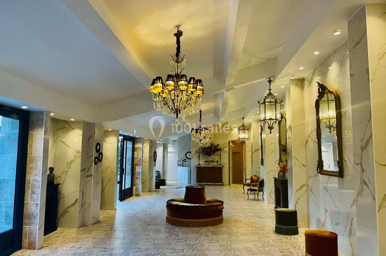 Hall spacieux avec lustres élégants, murs en marbre clair, miroirs dorés et sièges circulaires au centre.