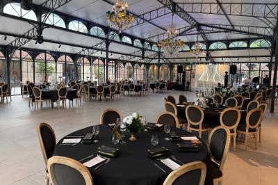 Terrasse extérieure avec tables, chaises, parasol, plantes et vue sur un bâtiment vitré sous un ciel dégagé.