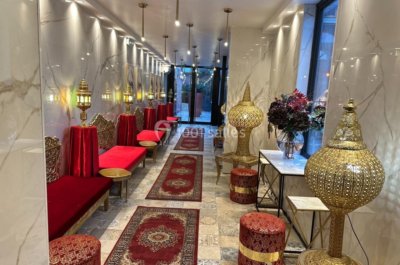 Salon décoré dans un style oriental avec banquettes rouges, tapis persans, lanternes dorées et fleurs sur une table.