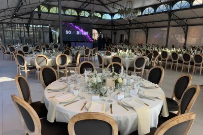 Terrasse extérieure avec tables, chaises, parasol, plantes et vue sur un bâtiment vitré sous un ciel dégagé.