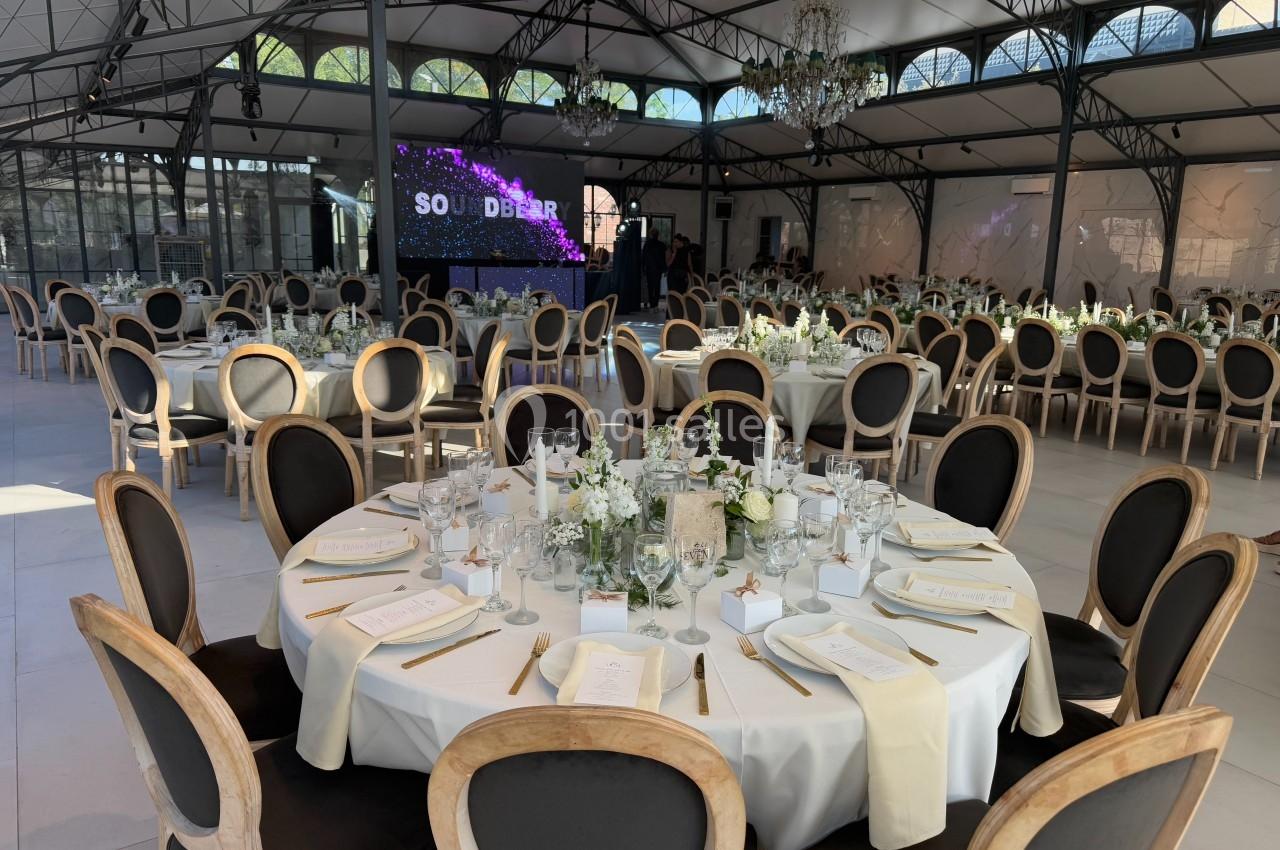 Salle de réception élégante avec tables rondes dressées, décor floral et écran lumineux en arrière-plan.