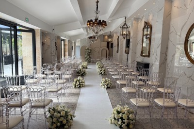 Terrasse extérieure avec tables, chaises, parasol, plantes et vue sur un bâtiment vitré sous un ciel dégagé.