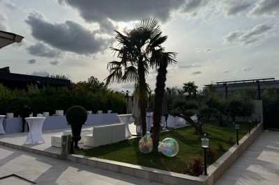 Terrasse extérieure avec tables, chaises, parasol, plantes et vue sur un bâtiment vitré sous un ciel dégagé.