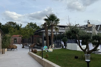 Terrasse extérieure avec tables, chaises, parasol, plantes et vue sur un bâtiment vitré sous un ciel dégagé.