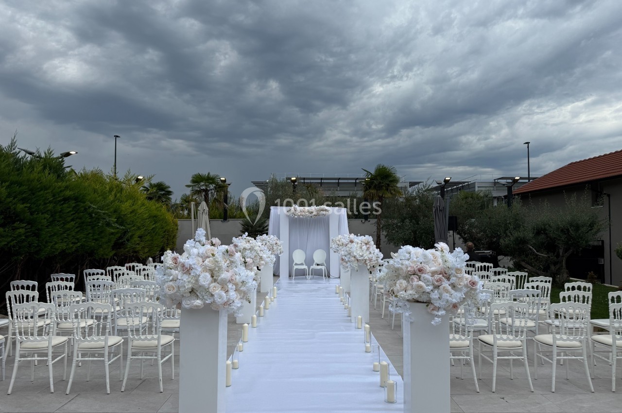 Allée centrale décorée de fleurs blanches menant à un autel extérieur sous un ciel nuageux.