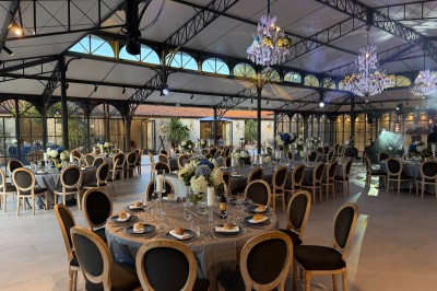 Terrasse extérieure avec tables, chaises, parasol, plantes et vue sur un bâtiment vitré sous un ciel dégagé.