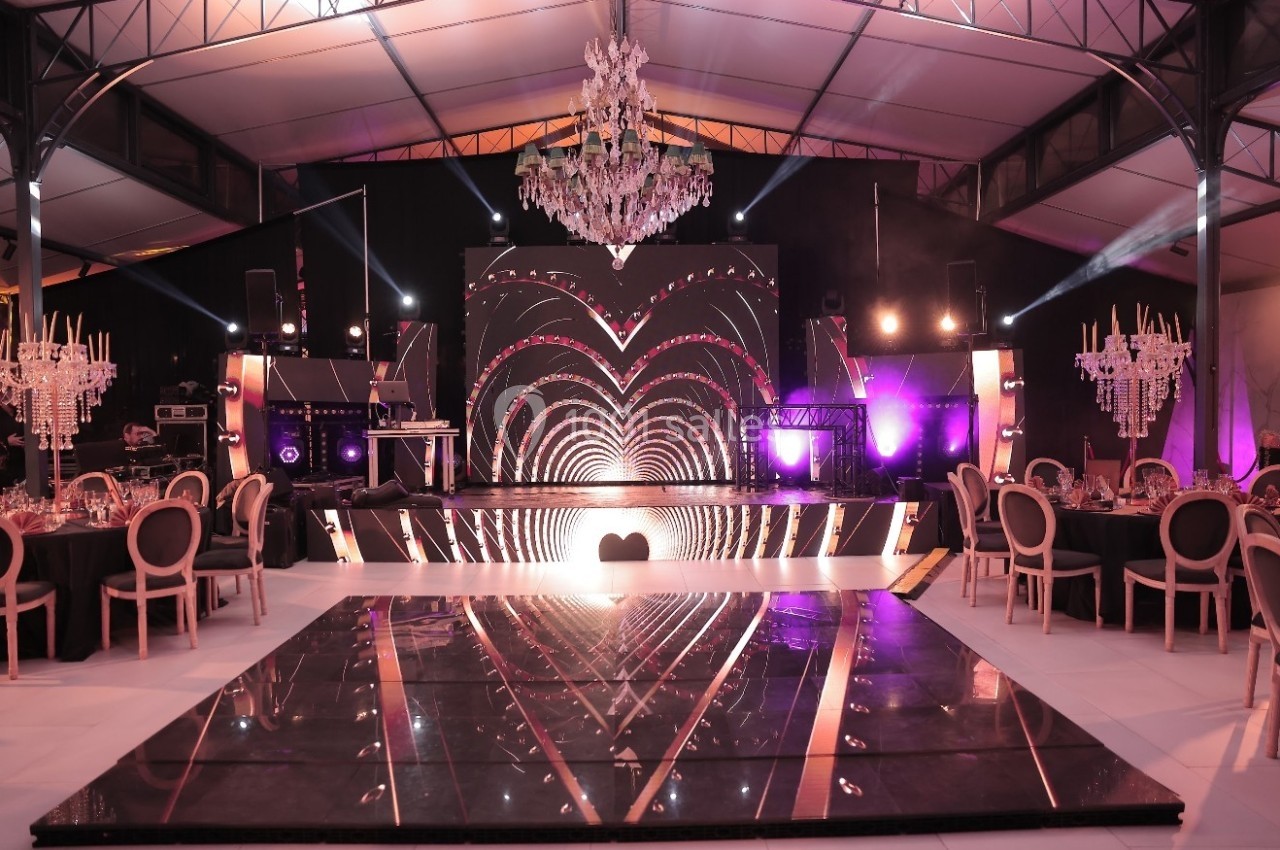 Salle de réception décorée avec un éclairage rose, un lustre central et une scène ornée de motifs lumineux en cœur.