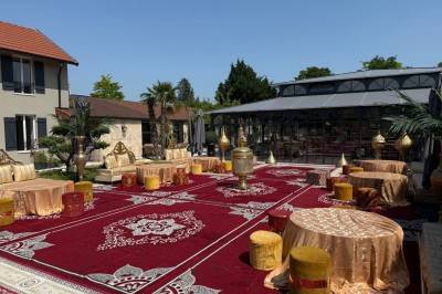 Terrasse extérieure avec tables, chaises, parasol, plantes et vue sur un bâtiment vitré sous un ciel dégagé.