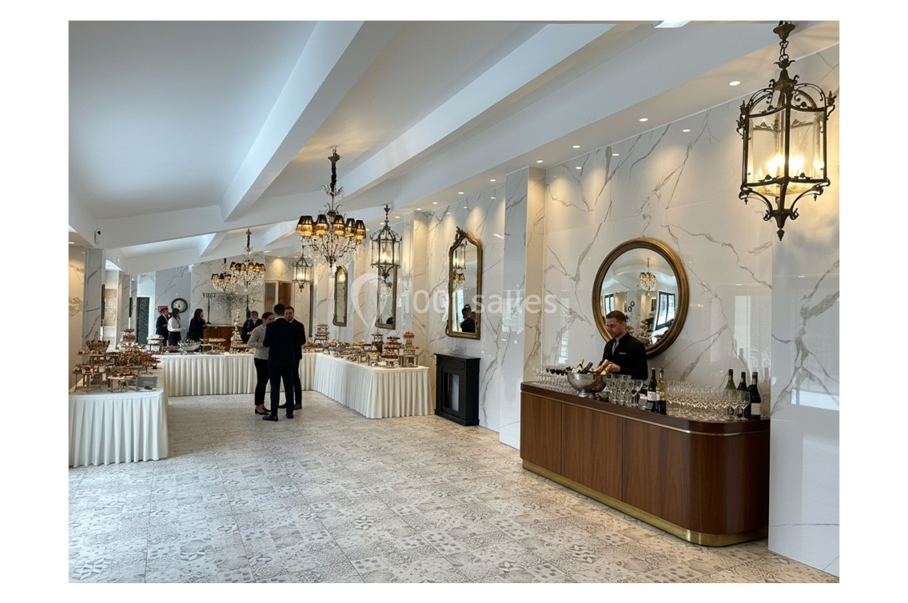 Salle élégante avec tables de buffet garnies, lustres suspendus, miroirs ronds et un serveur près d'un bar.