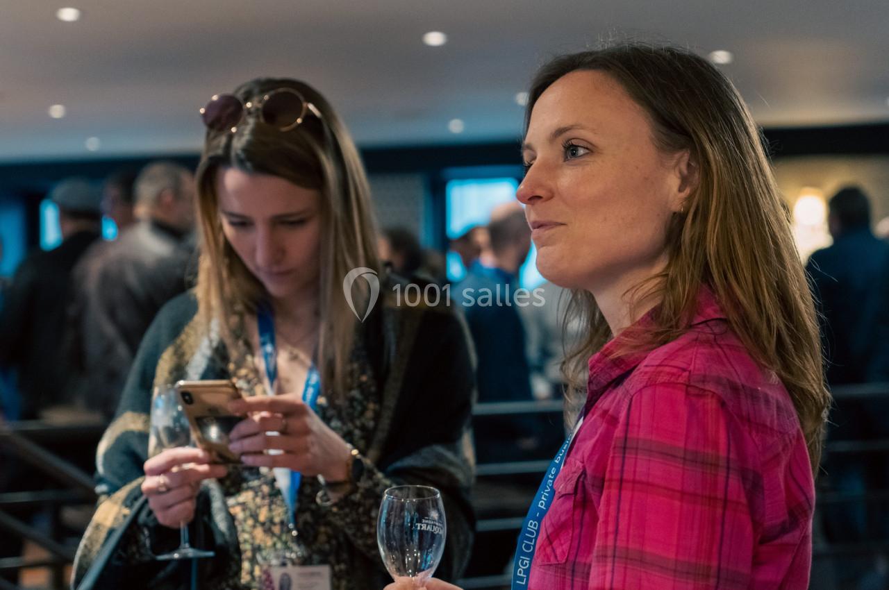 Deux femmes discutent lors d'un événement, l'une tenant un verre et l'autre regardant son téléphone.