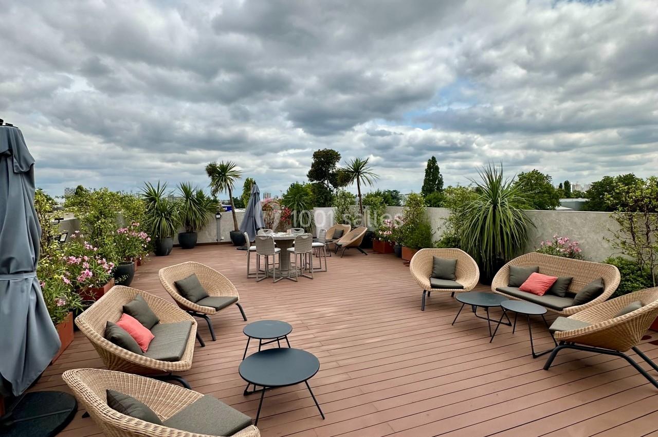 Terrasse en bois avec fauteuils, tables basses, plantes en pots et ciel nuageux en arrière-plan.