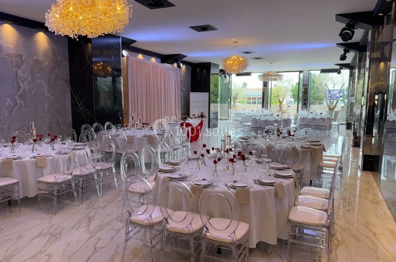 Salle de réception élégante avec tables rondes dressées, chaises transparentes et décorations lumineuses modernes.
