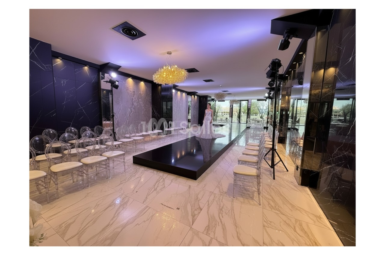 Salle élégante avec podium central, chaises transparentes alignées et éclairage tamisé sous un lustre doré.