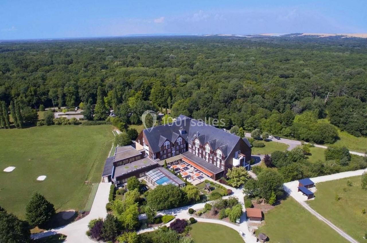 Vue aérienne d'un grand bâtiment entouré de verdure, avec une piscine et des chemins dans un paysage rural.