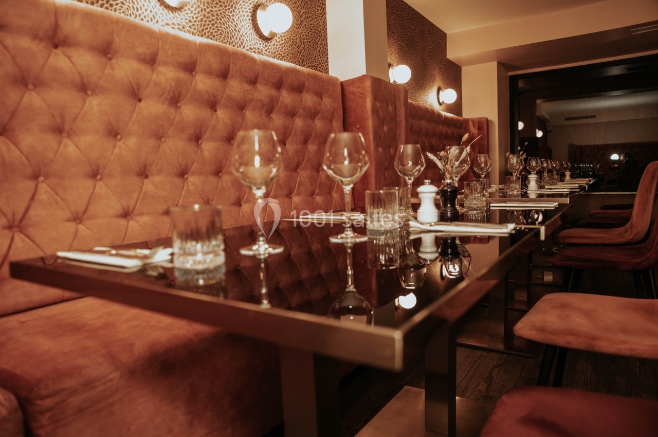 Salle de restaurant avec tables en verre, chaises rembourrées et verres disposés pour un service.