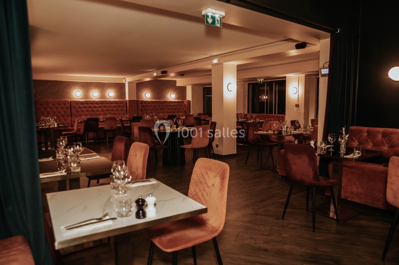 Salle de restaurant élégante avec tables dressées, chaises rembourrées et éclairage tamisé.