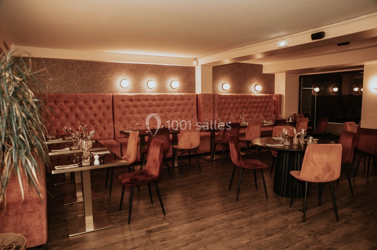 Salle de restaurant élégante avec tables dressées, chaises en velours rouge et éclairage tamisé.