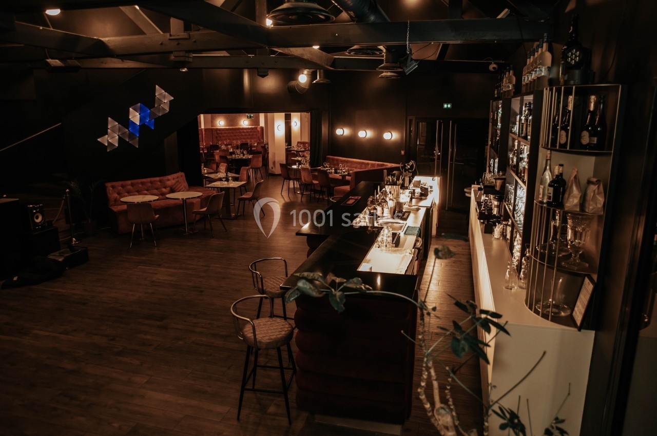 Intérieur d'un bar élégant avec un comptoir éclairé, des tables et une ambiance tamisée.