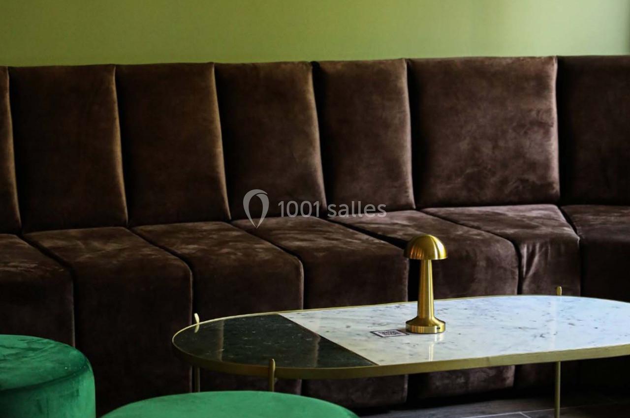 Canapé en velours marron devant une table basse en marbre avec une lampe dorée, dans une pièce aux tons verts.