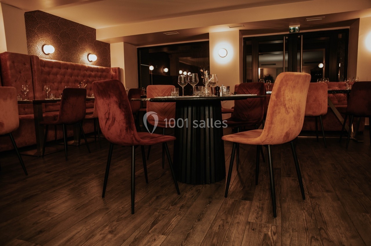 Salle de restaurant élégante avec chaises en velours, tables dressées et éclairage tamisé sur parquet en bois.