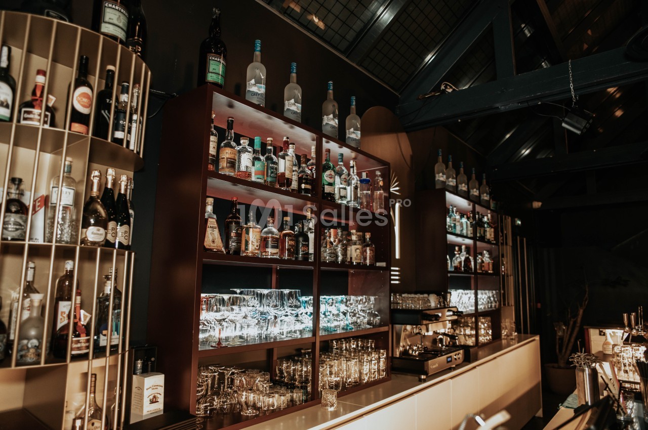 Étagères remplies de bouteilles d'alcool et de verres dans un bar à l'ambiance tamisée et moderne.