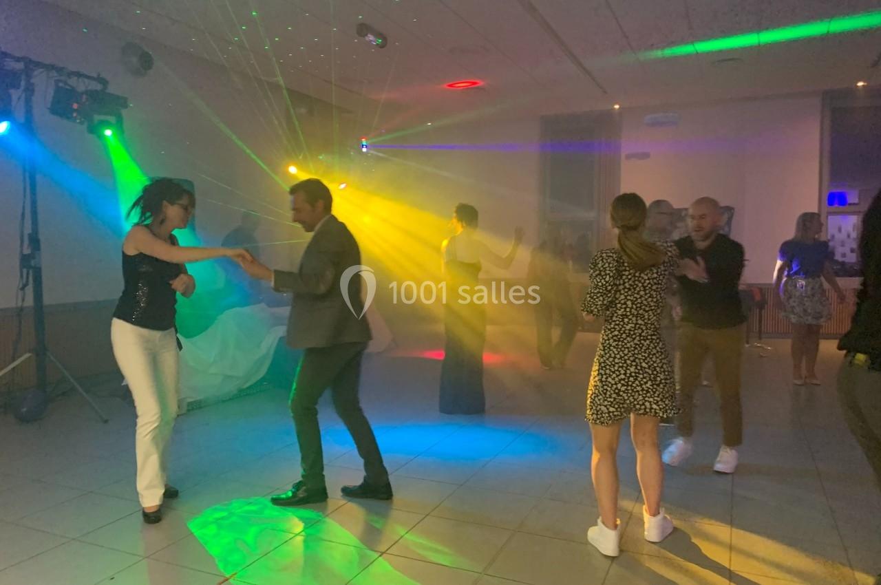 Des personnes dansent sous des lumières colorées dans une salle sombre lors d'une soirée festive.