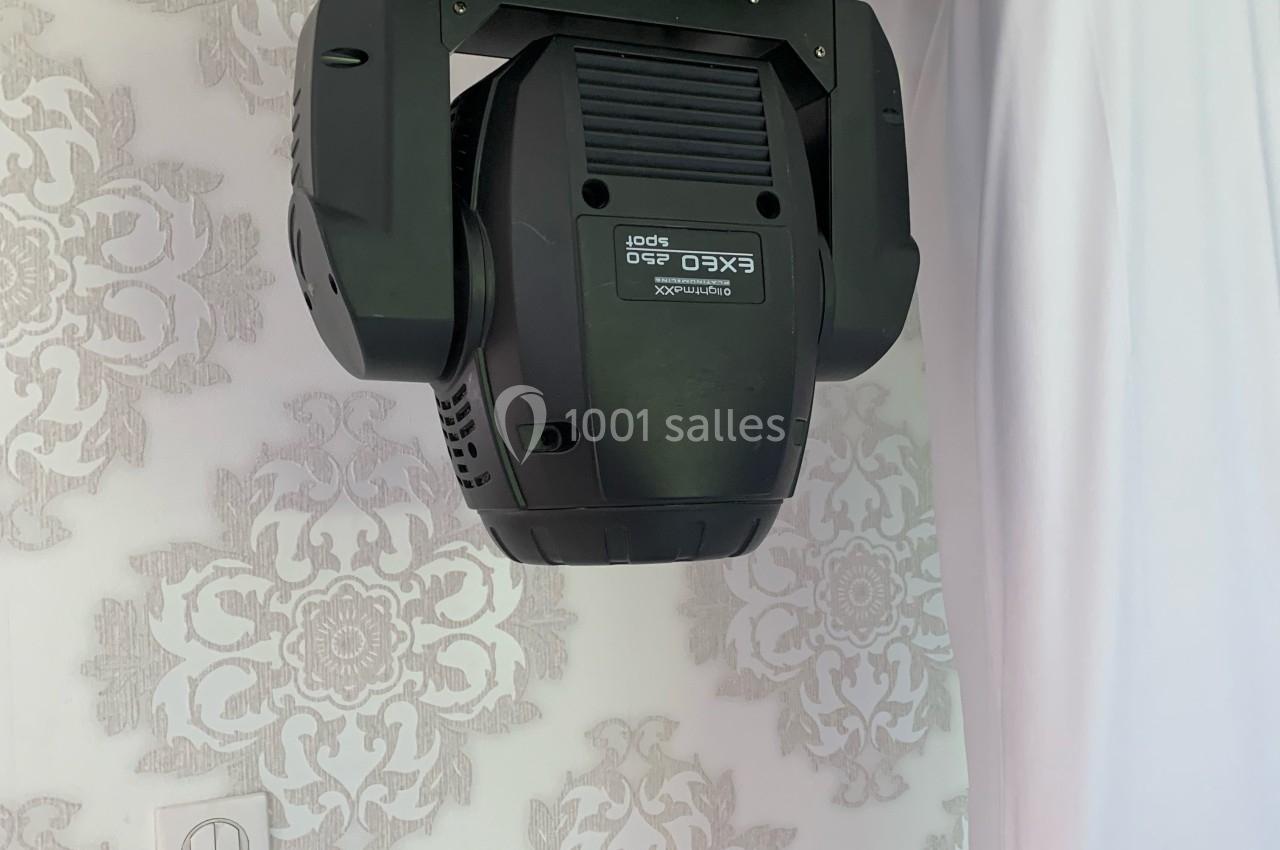 Projecteur d'éclairage suspendu à une structure métallique, devant un mur décoré de motifs floraux.