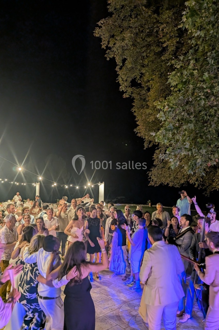 Groupe de personnes dansant en plein air sous des guirlandes lumineuses, entouré d'arbres et d'une ambiance festive nocturne.
