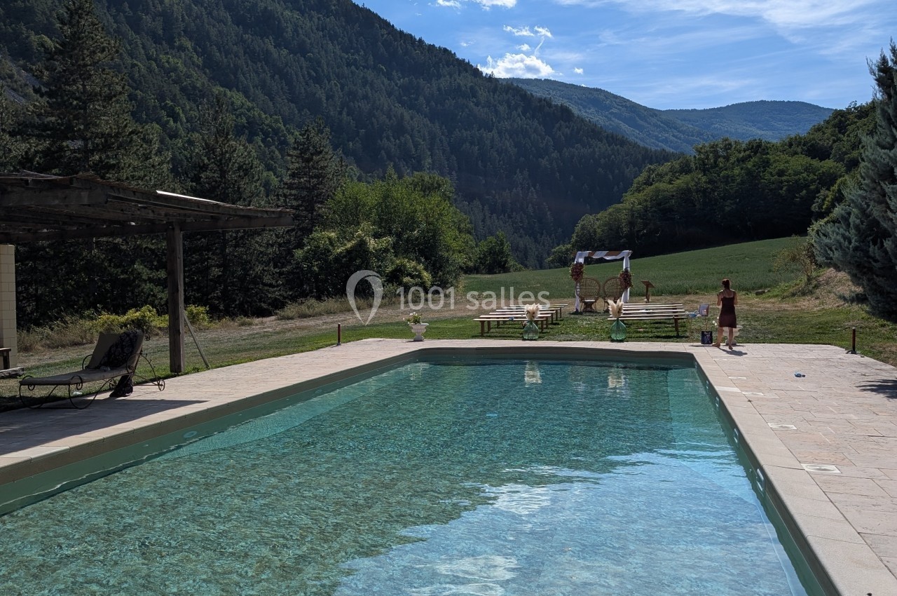 Piscine extérieure entourée de montagnes et de verdure, avec une pergola et des chaises longues à proximité.