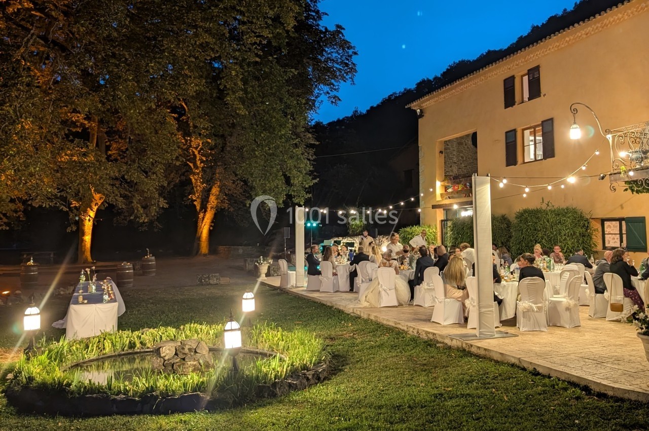 Dîner en plein air dans un jardin éclairé, avec des convives assis à des tables près d'une maison au crépuscule.