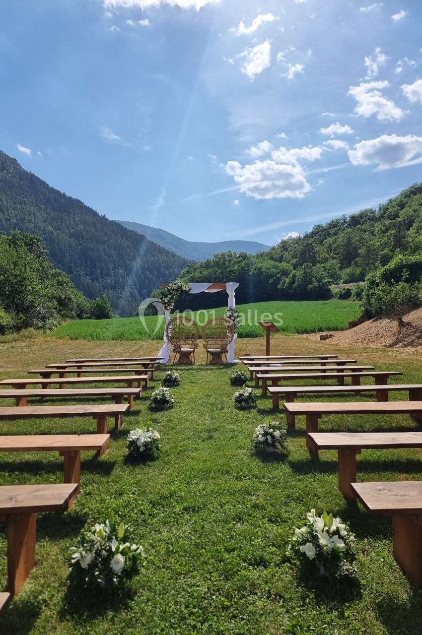Allée bordée de bancs en bois menant à une arche décorée pour une cérémonie en plein air, entourée de montagnes verdoyantes.