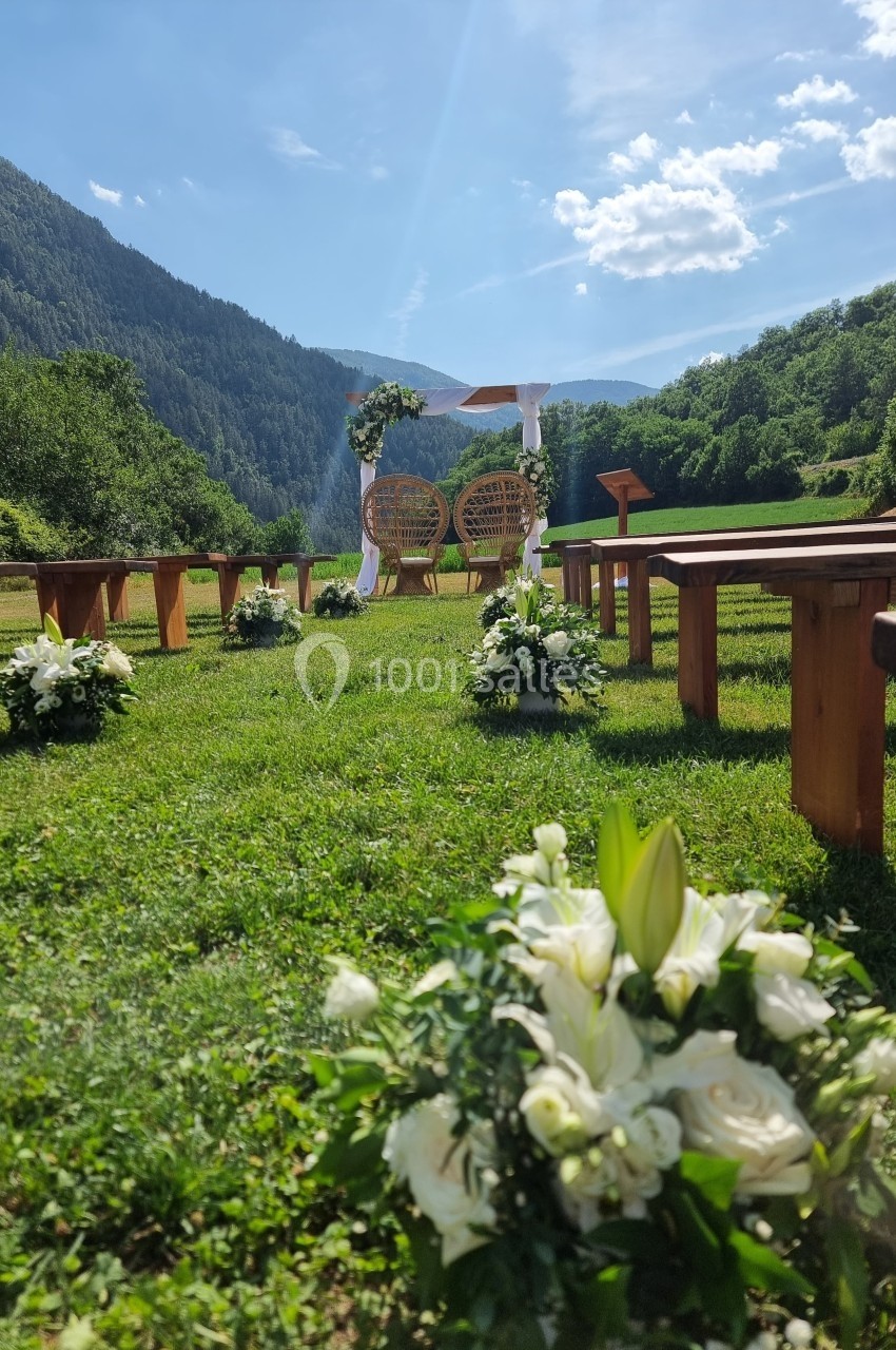 Cérémonie de mariage en plein air avec arche fleurie, bancs en bois et montagnes en arrière-plan.
