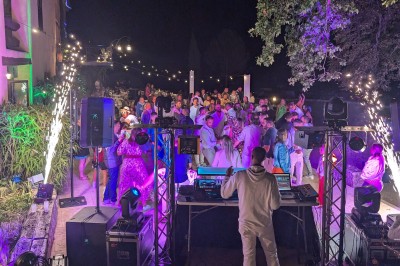 Un homme en costume parle devant une arche décorée de fleurs séchées, dans un cadre naturel avec des montagnes et des arbres.