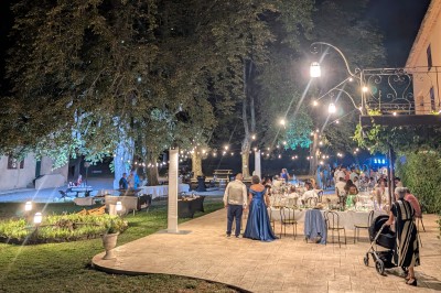 Un homme en costume parle devant une arche décorée de fleurs séchées, dans un cadre naturel avec des montagnes et des arbres.