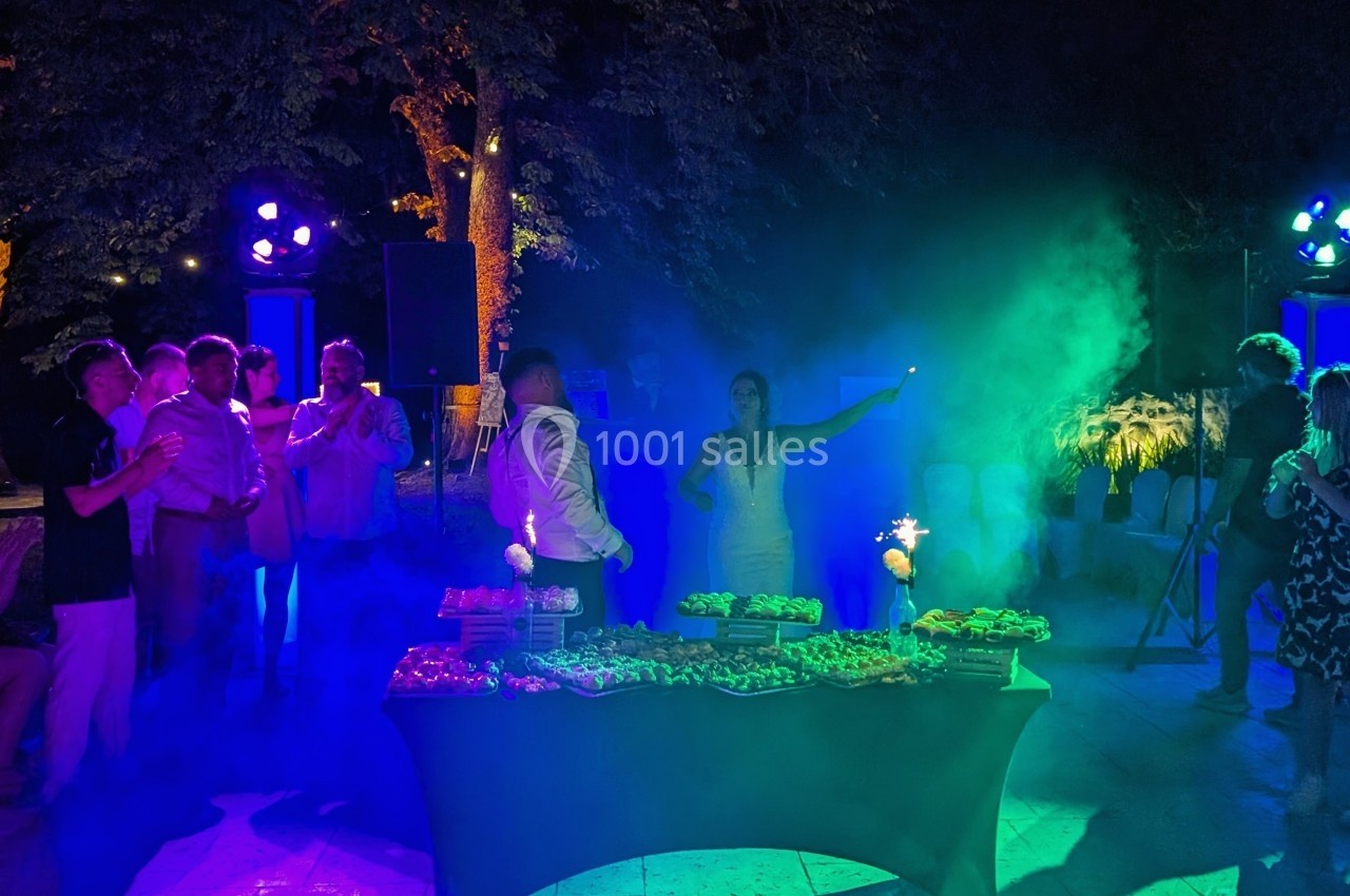 Des invités rassemblés autour d'une table garnie de plats, éclairés par des lumières colorées dans une ambiance nocturne…