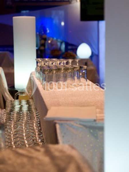 Rangée de verres alignés sur une table recouverte d'une nappe blanche dans un environnement éclairé.