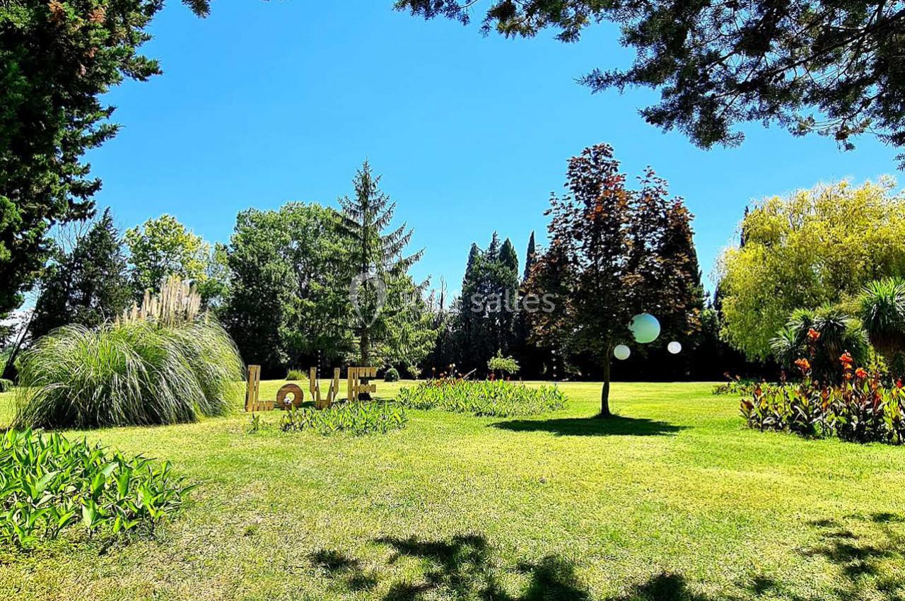 Pelouse verdoyante avec des arbres, des fleurs colorées et des lettres formant ’LOVE’ au milieu d'un parc ensoleillé.