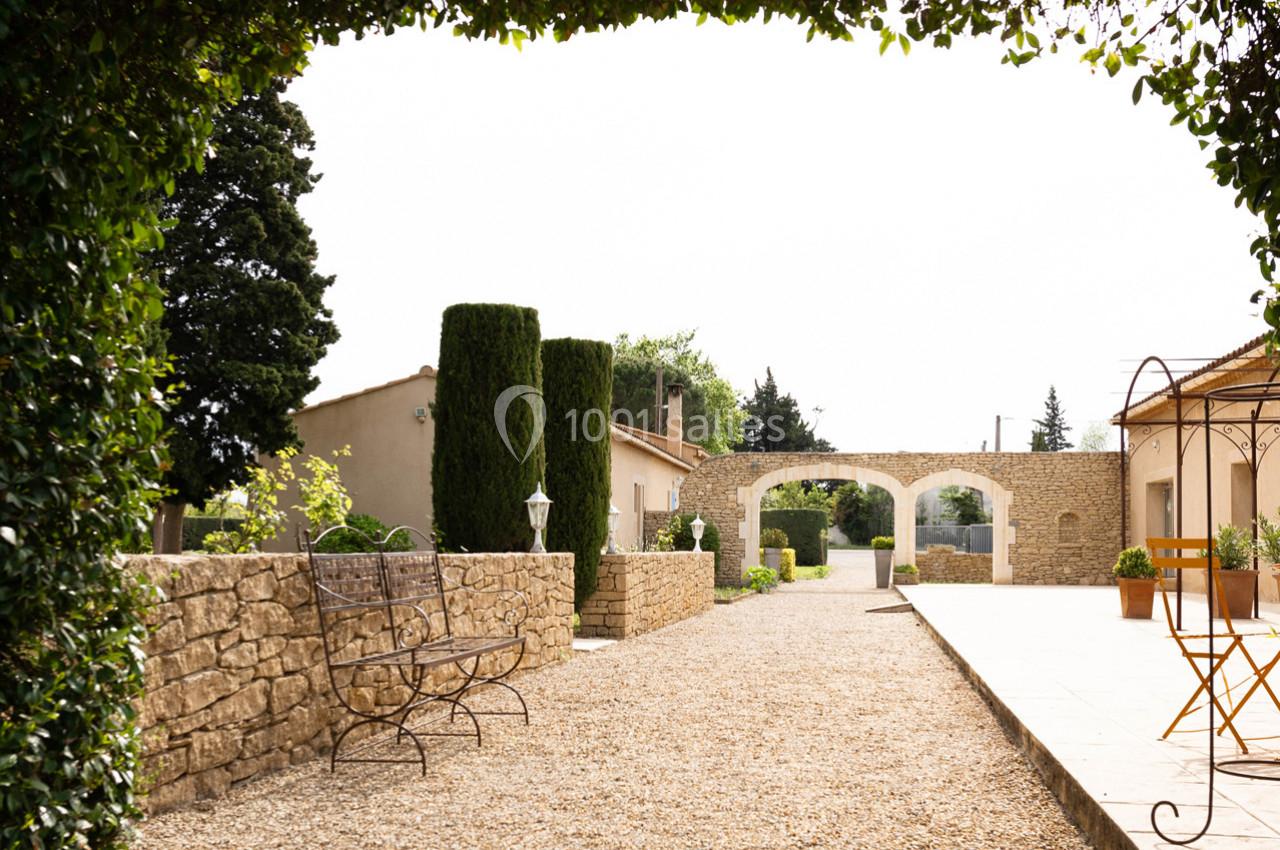 Cour extérieure avec banc en fer forgé, allée gravillonnée, arches en pierre et végétation méditerranéenne.