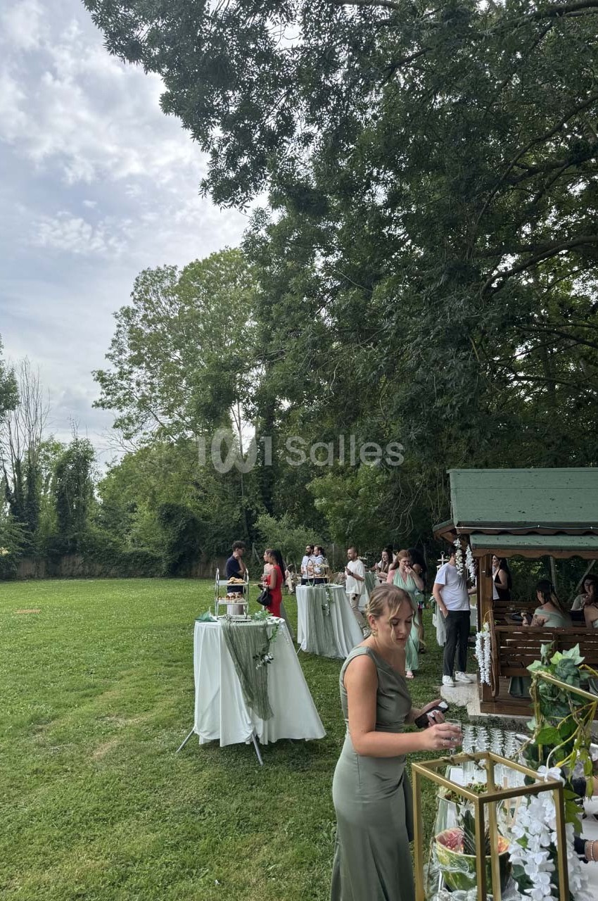 Personnes rassemblées dans un jardin près d'un kiosque en bois, avec des tables décorées pour un événement en plein air.