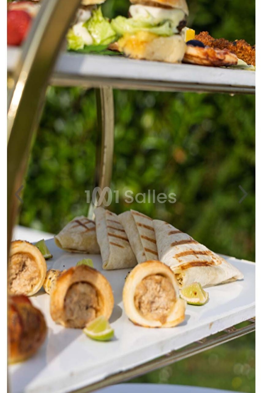 Plateau de service avec wraps grillés, feuilletés farcis et mini-burgers, disposés sur deux étages en extérieur.