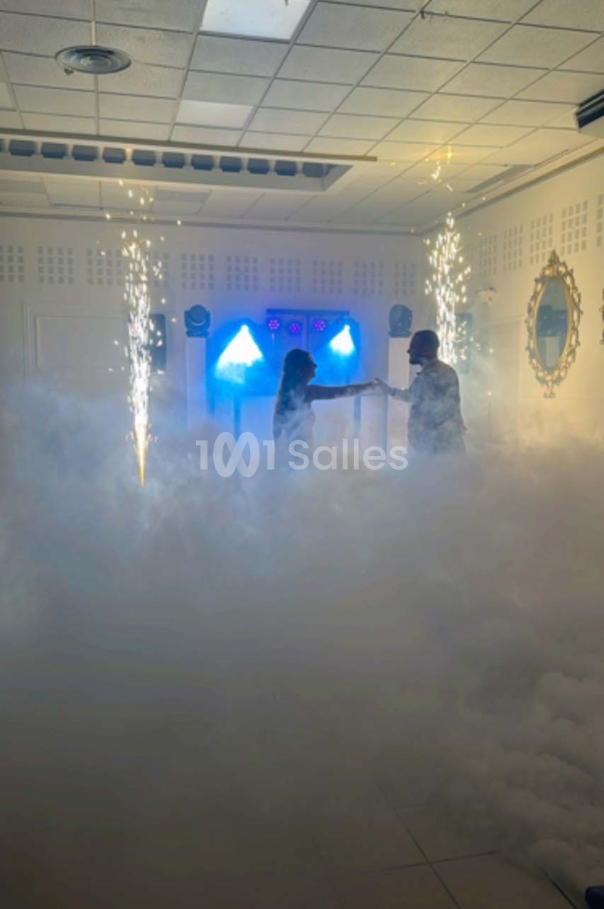 Deux personnes dansent au milieu de la fumée et d'effets lumineux avec des étincelles dans une salle fermée.
