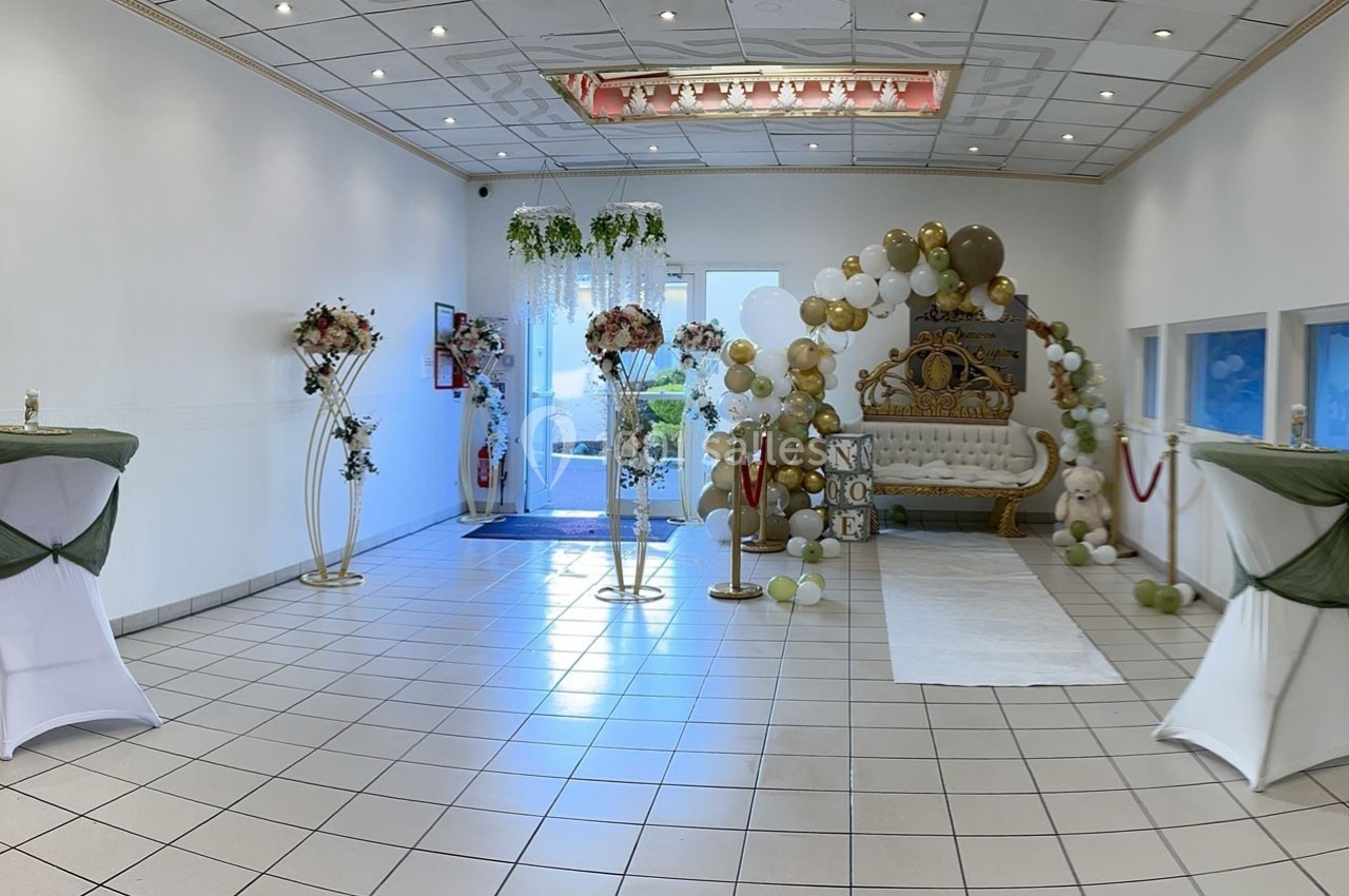 Salle décorée pour un événement avec arche de ballons, canapé doré, tables hautes et fleurs.