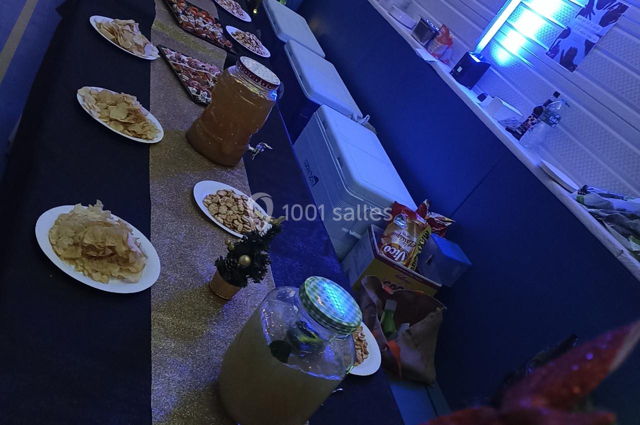 Table décorée avec nappes noires et dorées, garnie de plats variés et boissons, dans une salle éclairée par des lumières…