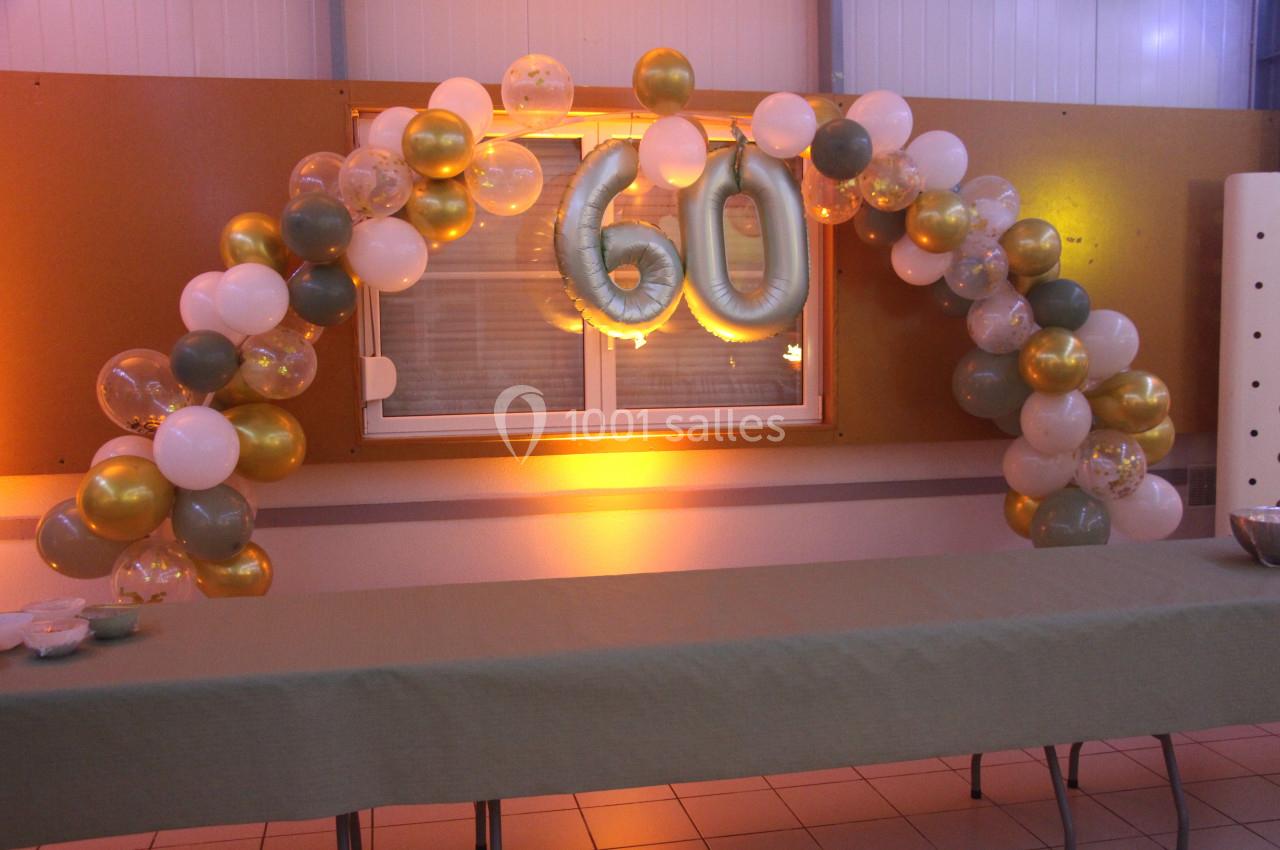 Décoration d'anniversaire avec arche de ballons dorés, blancs et verts, et le chiffre 60 en ballons argentés.