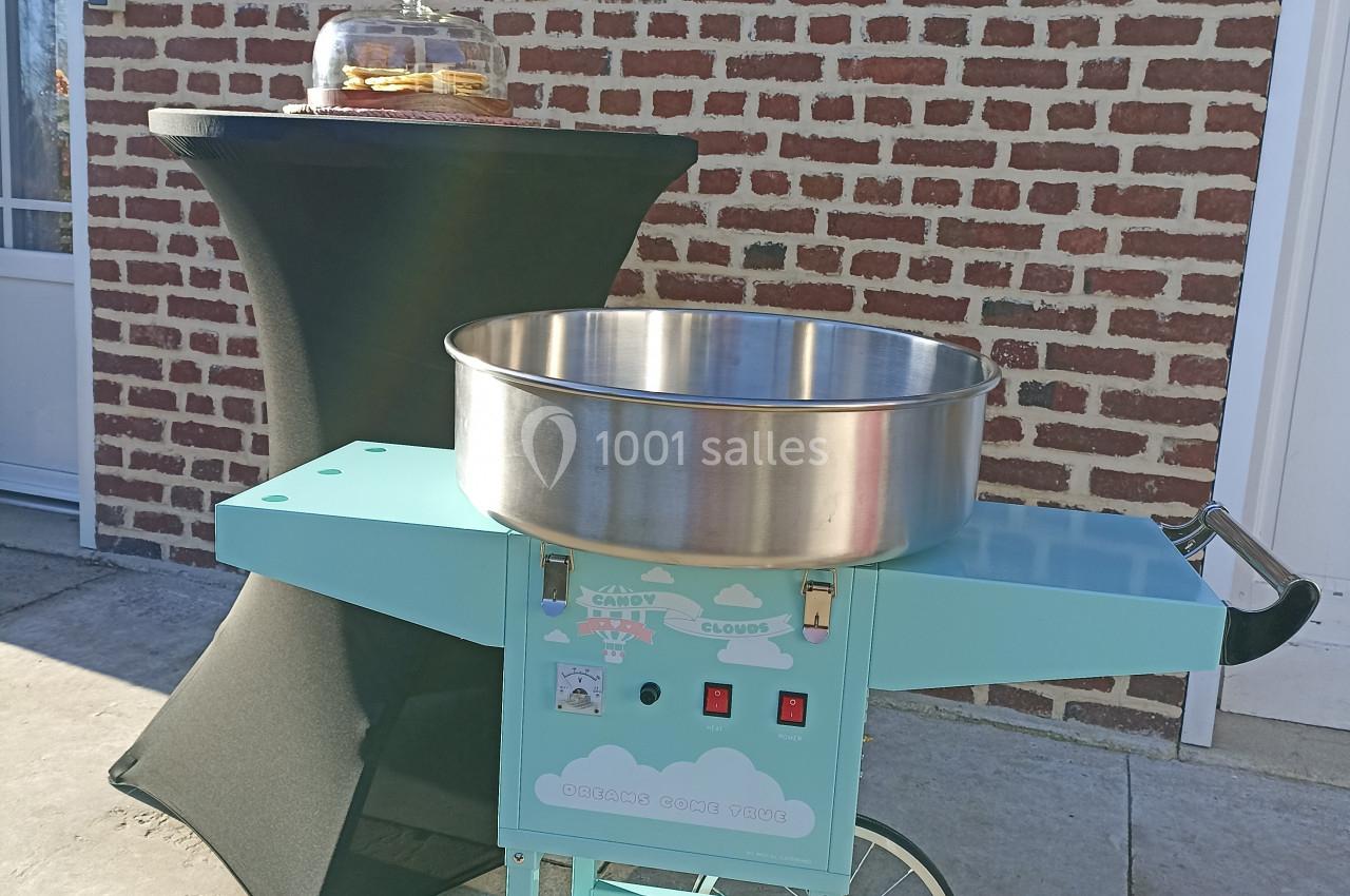 Chariot bleu de machine à barbe à papa devant une table haute noire avec une cloche contenant des biscuits.