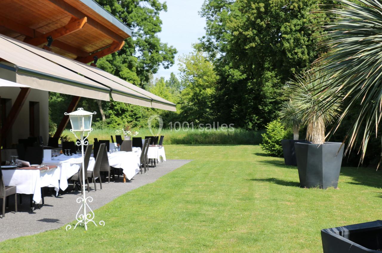 Terrasse d'un restaurant avec tables dressées sous un auvent, entourée de verdure et de grands arbres.