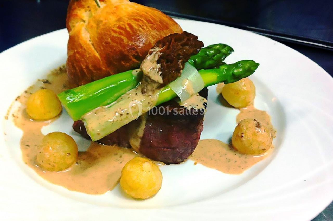Assiette gastronomique avec filet de viande, asperges, morille, pommes dauphines et sauce, servie sur une assiette blanche.